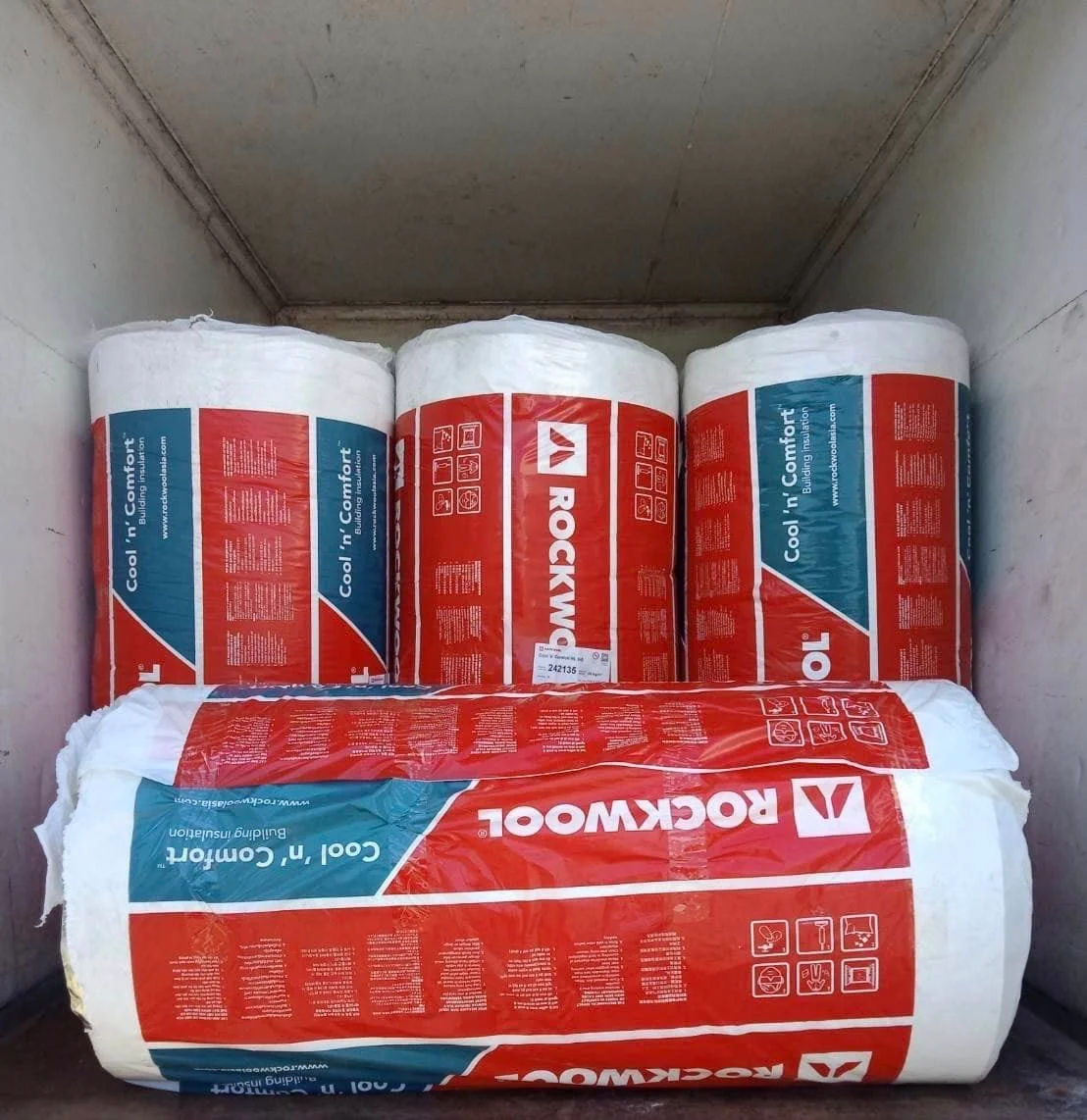 Four rolls of red-and-white Rockwool insulation stacked inside a truck or container
