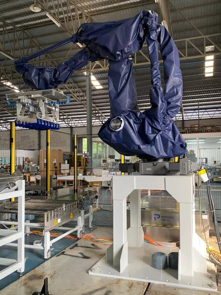 A blue robotic arm in an industrial setting is mounted on a white base, surrounded by machinery. The logo